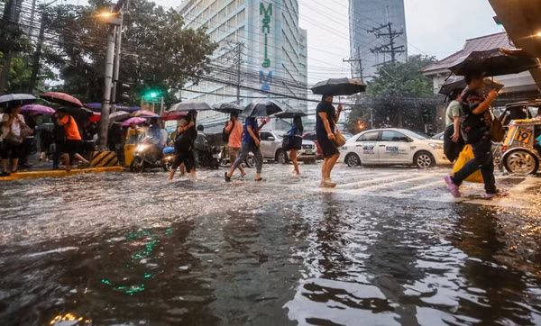 Người dân đi trên đường phố ngập nước do mưa ở thủ đô Manila (Philippines). Ảnh: Rappler.
