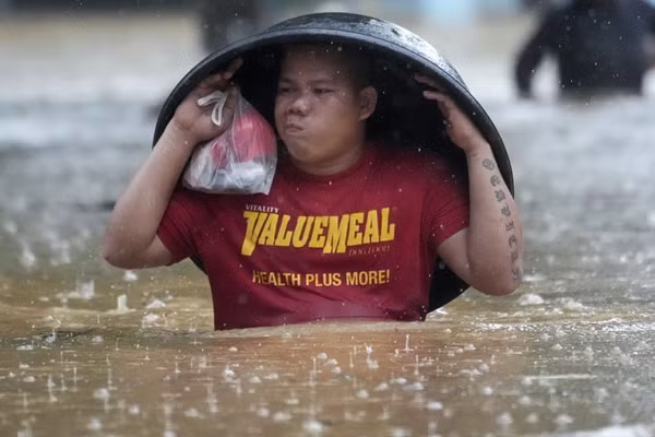 Một người dân ở tỉnh Rizal (Philippines) dùng chậu giặt để che mưa khi lội trên con phố ngập nước do ảnh hưởng của bão Yagi. Ảnh: Aaron Favila/ AP.
