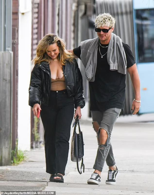 Abbie Chatfield diện áo khoác da buông cúc, lộ rõ áo bra màu nâu trễ nải, phô vòng một nảy nở.