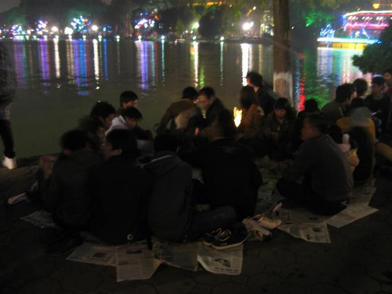 Nhóm bạn trẻ này trải giấy báo ngồi ngay ven hồ để chờ đón màn bắn pháo hoa. Ảnh : Văn Việt