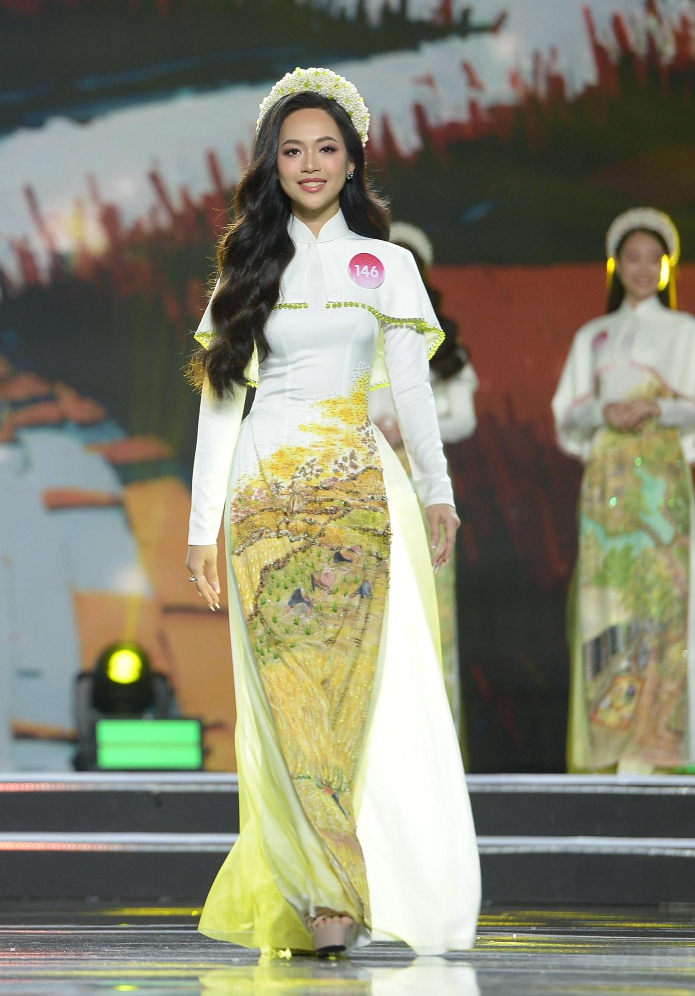 Á hậu 1 Trịnh Thùy Linh thể hiện những bước catwalk uyển chuyển trong tà áo dài thướt tha thuộc bộ sưu tập Bức họa đồng quê của NTK Bảo Bảo. Dù nằm trong nhóm thí sinh đầu tiên trình diễn, nữ sinh Thanh Hóa tự tin hoàn thành xuất sắc phần thi.