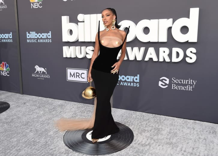 Tại Lễ trao giải âm nhạc Billboard vào tháng 5, Doja Cat chọn trang phục lấy cảm hứng từ khoa học viễn tưởng để phù hợp với album Planet Her. Đó là chiếc váy đen ôm sát đường cong cơ thể có hai chiếc sừng nhô lên, phần cổ khoét bạo. Ngoài ra, phụ kiện đi kèm là chiếc ví hình sao Thổ bằng vàng. Bộ cánh đến từ bộ sưu tập Planet Schiaparelli mang chủ đề vũ trụ của Daniel Roseberry, ra mắt tại Tuần lễ Thời trang cao cấp Paris vào tháng Giêng. Ảnh: AP.