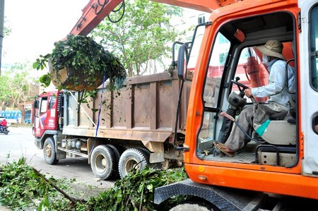 Xe máy đào và xe tải của một doanh nghiệp tình nguyện dọn dẹp đường phố sau bão