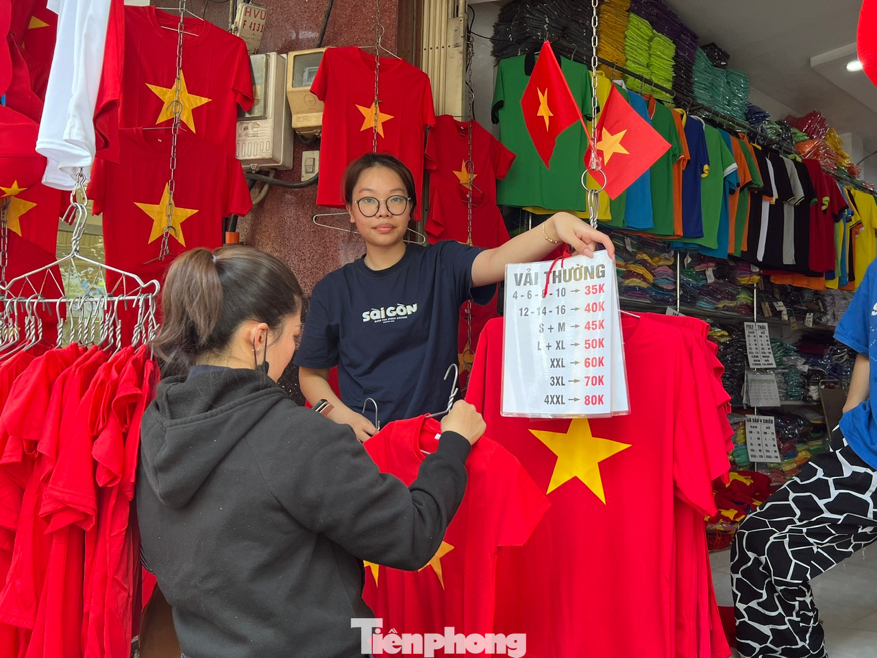 Cửa hàng treo bảng giá công khai để khách hàng dễ dàng chọn lựa, giá mềm chỉ từ 50.000 đồng/áo thun, lá cờ 10.000 đồng/cái, mũ nón khoảng 30.000 đồng/cái tùy loại.