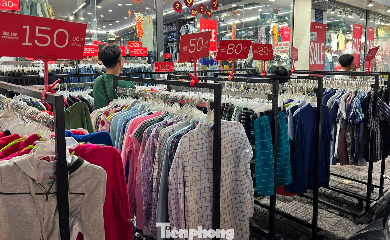 Một cửa hàng thời trang lớn bày cả quần áo ra vỉa hè, treo bảng giảm giá đỏ rực để thu hút khách nhưng cũng chỉ có một vài khách ghé qua xem hàng...