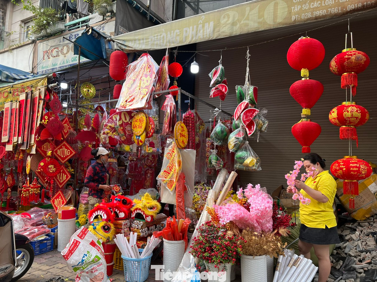 Những tiểu cảnh để trang trí góc xuân ngày Tết như bánh chưng bánh tét bằng xốp, đầu lân, quạt nan, hoa mai hoa đào bằng giấy... bày tràn trước cửa tiệm.