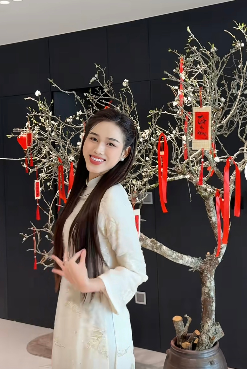 Hoa hậu Đỗ Thị Hà cắm một cành đào cỡ lớn trong không gian phòng khách để chuẩn bị đón Tết. Người đẹp trang trí cho cành đào bằng những đồ decor tông màu đỏ cầu kỳ, nổi bật. Hoa hậu Việt Nam 2020 diện áo dài, hào hứng chụp ảnh bên cành đào sau khi được trang trí lộng lẫy.