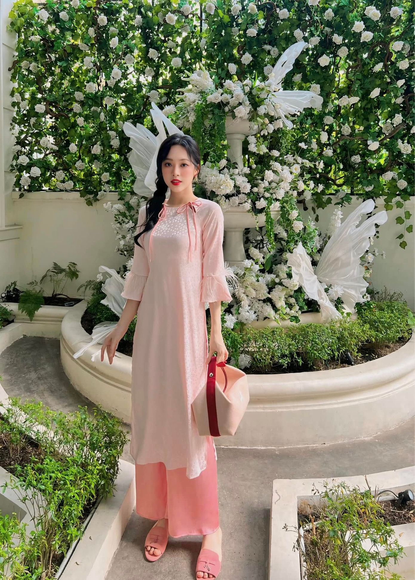 Á hậu Trịnh Thùy Linh chọn áo dài tông màu hồng pastel dịu dàng. Cô khéo léo phối cùng túi xách, dép bệt cùng tông màu. Người đẹp Thanh Hóa được khen khéo léo chọn áo dài tôn số đo ba vòng chuẩn.