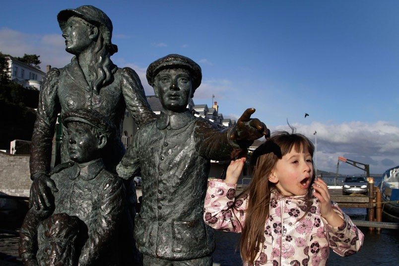Bé gái đứng bên bức tượng tưởng niệm chào đón đoàn tàu chở 1.309 hành khách tại Cobh.