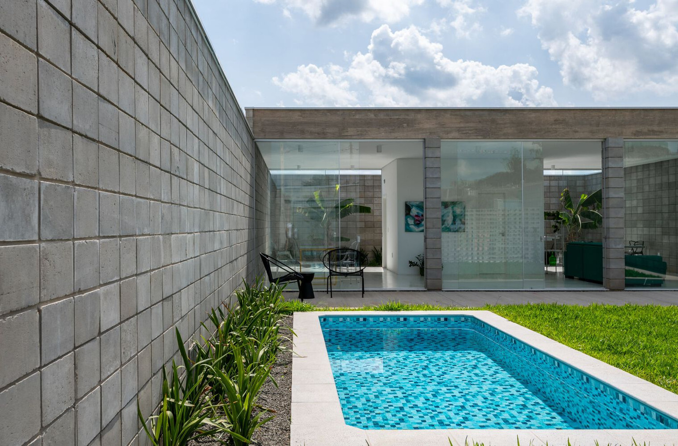 Phần phía trước của ngôi nhà được chia thành ba không gian lớn: Một không gian bê tông, đủ để đậu hai xe; một không gian khác bằng sỏi, nơi kiến trúc sư lắp đặt một thùng chứa đa năng; và cuối cùng là bãi cỏ lớn có hồ bơi.