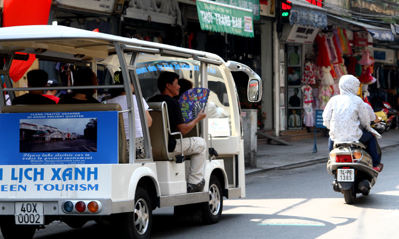 Khách du lịch ngồi trên xe điện vẫn không ngơi tay quạt mạt để xua hơi nóng