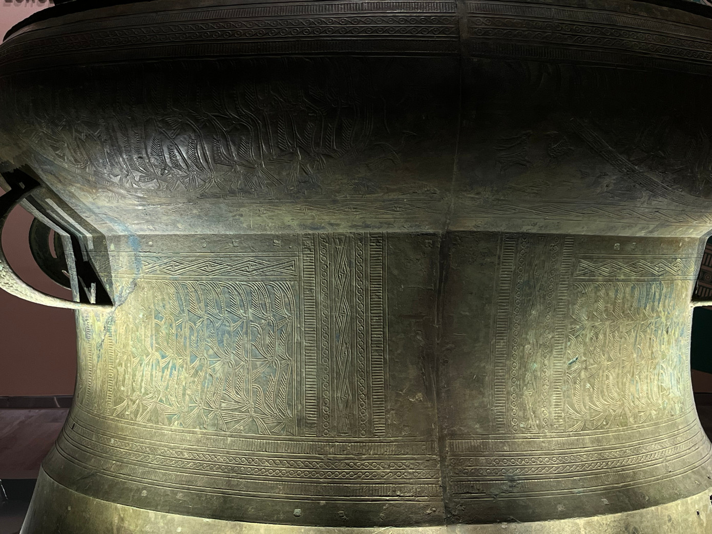 Cảnh sinh hoạt được thể hiện trên mặt trống qua hình tượng người hóa trang xen kẽ bốn ngôi nhà sàn mái cong, mái rủ. Một đường vành trang trí hình chim lạc xoay ngược chiều kim đồng hồ. Diềm ngoài của mặt trống đính 4 tượng cóc nổi ngược chiều kim đồng hồ. Phía trên tang trống có các vành trang trí hoa văn vòng tròn, vạch ngắn. Trống có hai đôi quai kép trang trí nổi văn hình bông lúa. Chân trống không có hoa văn trang trí.