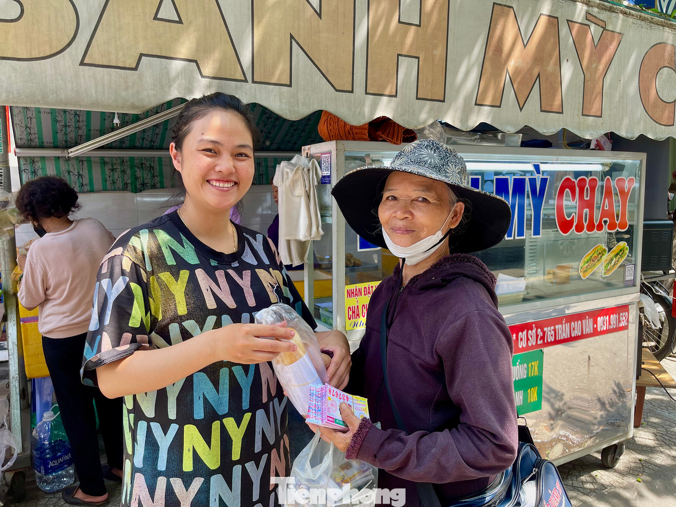 Cô Tâm (bên phải) vui vẻ nhận ổ bánh mì “treo” từ chị Thảo trong lúc mưu sinh bằng nghề bán vé số dạo. Ảnh: Ngọc Thắm Cô Tâm (bên phải) vui vẻ nhận ổ bánh mì “treo” từ chị Thảo trong lúc mưu sinh bằng nghề bán vé số dạo. Ảnh: Ngọc Thắm