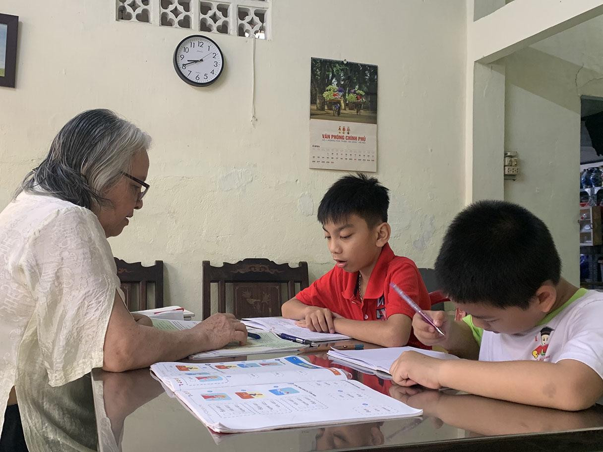 Hai bạn Huy Hoàng (áo đỏ) và Trung Kiên (áo trắng) ngoan ngoãn học tiếng Anh với bà Hương - ảnh Đ.T Hai bạn Huy Hoàng (áo đỏ) và Trung Kiên (áo trắng) ngoan ngoãn học tiếng Anh với bà Hương - ảnh Đ.T