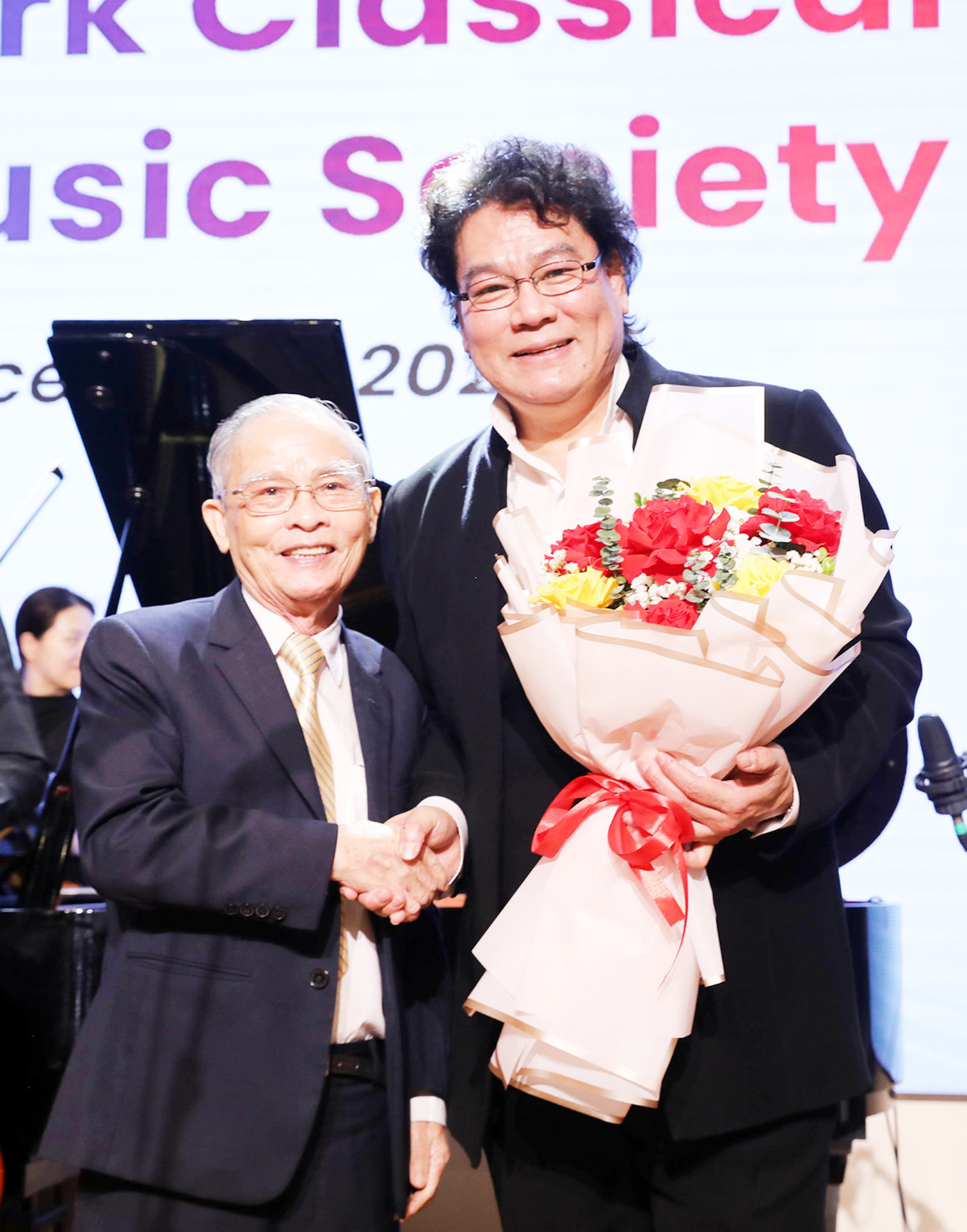 Chủ tịch Hội đồng nhà trường - AHLĐ, NGƯT Lê Công Cơ (bên trái) tặng hoa cùng lời chúc Giáng sinh và năm mới đến các nghệ sĩ đến từ New York Classical Music Society