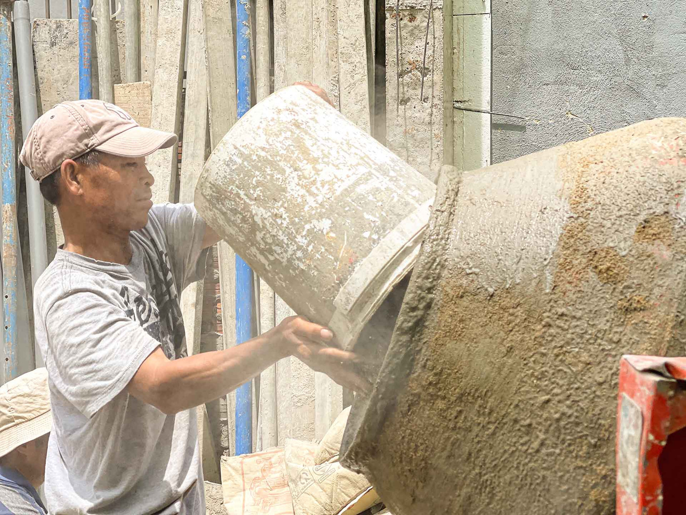 Bên cạnh đó là anh Hồ Duy, 42 tuổi, một phụ hồ đang cật lực làm công việc trộn bê tông. "Thời tiết thế này ai cũng muốn ở nhà, nhưng ở nhà thì tiền đâu để chăm lo cho gia đình. Nghĩ đến điều đó thì dù có nắng mưa cỡ nào cũng không làm khó được tôi” - anh Duy chia sẻ. (Ảnh: Thanh An)