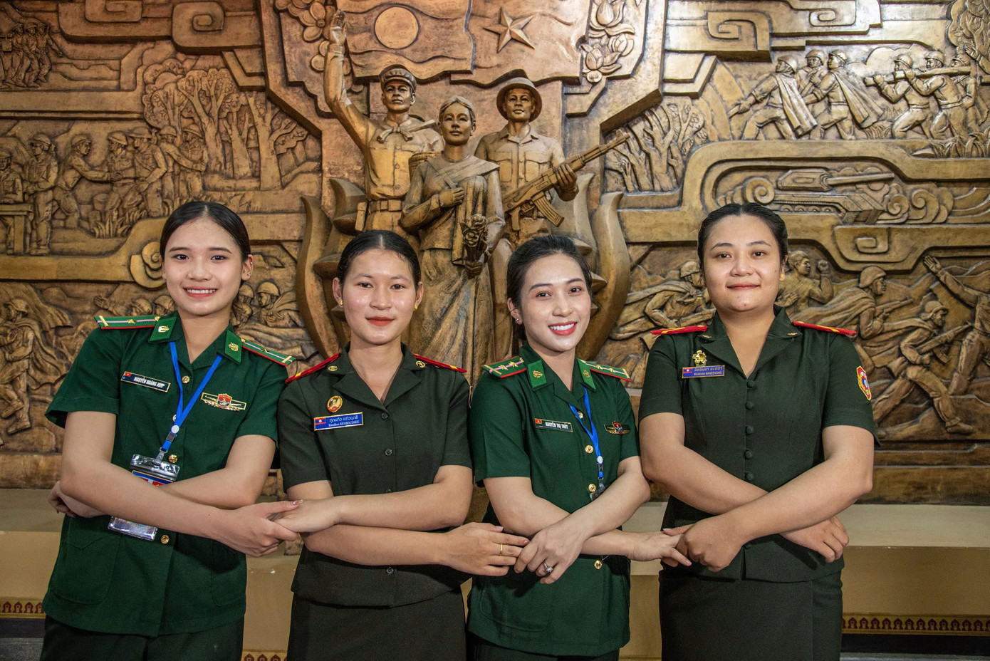 Các nữ quân nhân của Bộ đội biên phòng Việt Nam và Lào tay trong tay trước tượng đài khắc hình tượng người lính Việt Nam và Lào cùng chung một chiến hào dưới hai ngọn cờ Lào – Việt Nam tại Bảo tàng Liên minh chiến đấu Lào – Việt Nam. Ảnh: Văn Chương