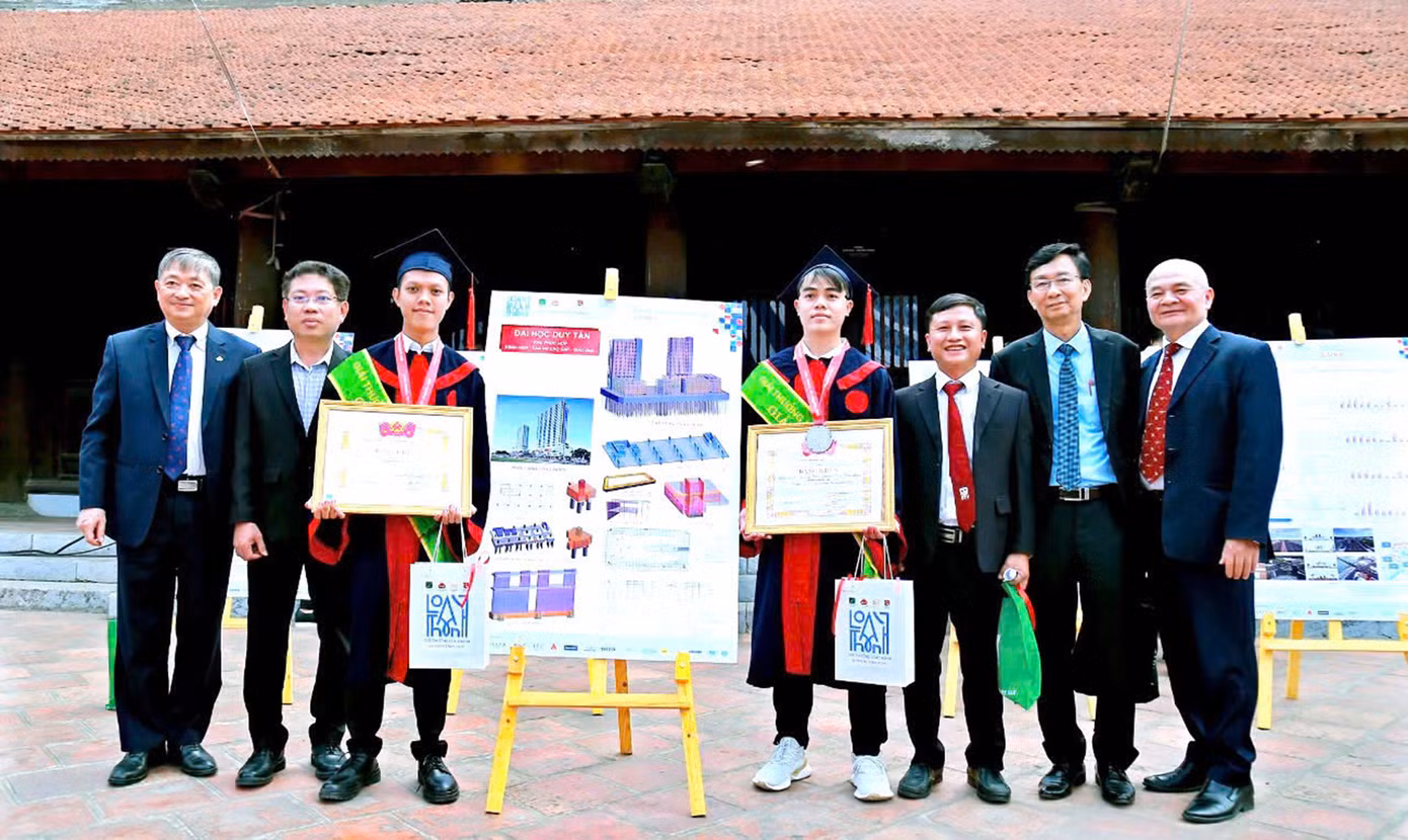 Hai sinh viên DTU chụp ảnh lưu niệm cùng các thầy cô bên Đồ án Tốt nghiệp đạt giải Nhì