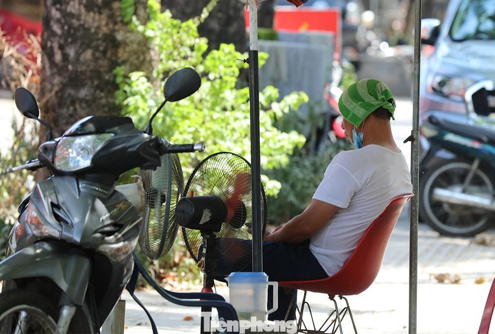 Bảo vệ một cửa hàng trên đường Nguyễn Trãi,quận Thanh Xuân với khăn đội đầu cùng 2 chiếc quạt phả thẳng vào người nhằm giảm nhiệt.