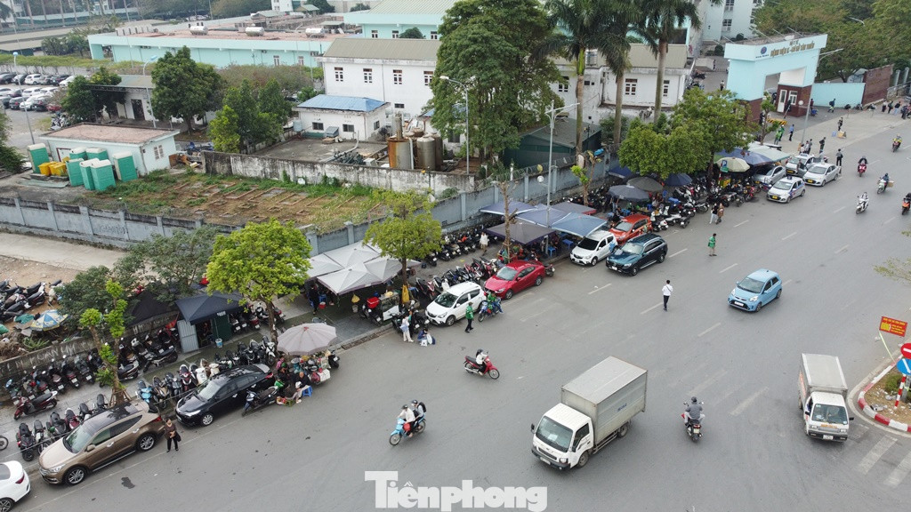 Nhân viên các bãi xe 'có phép' này vô tư đứng trên đường vẫy xe máy, ô tô gửi ở vỉa hè, lòng đường, sau đó thu tiền dịch vụ. Thậm chí họ trưng cả biển trông xe xuống lòng đường.