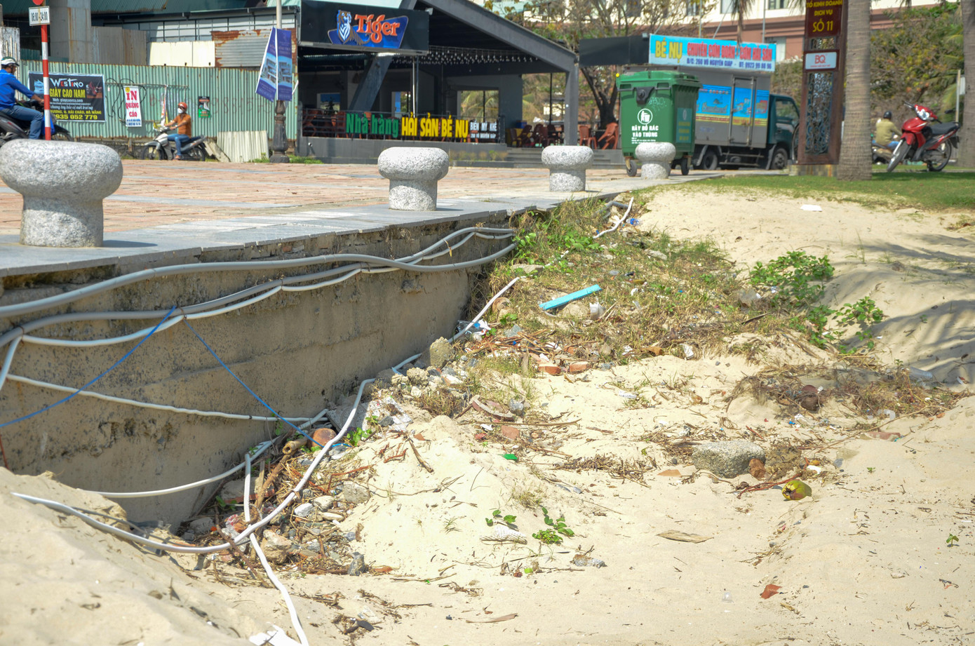 Sóng đánh toác bờ kè, lộ ra cả dây điện, dây cáp. Đá, rác...nằm ngổn ngang dưới hố sụt lún. Ảnh: Thái Lâm.