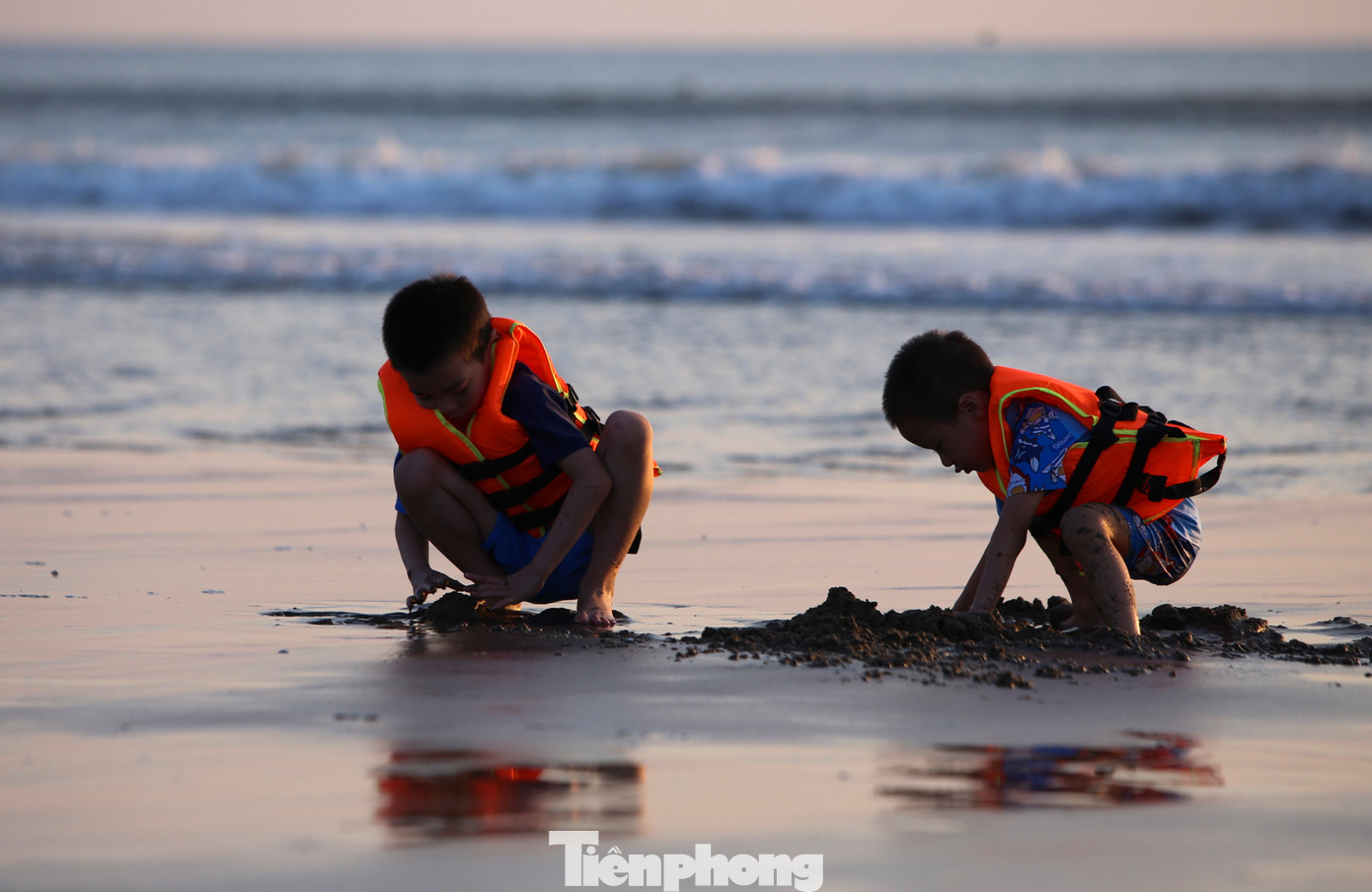 Những em nhỏ vui đùa xây lâu đài cát trên bãi biển.