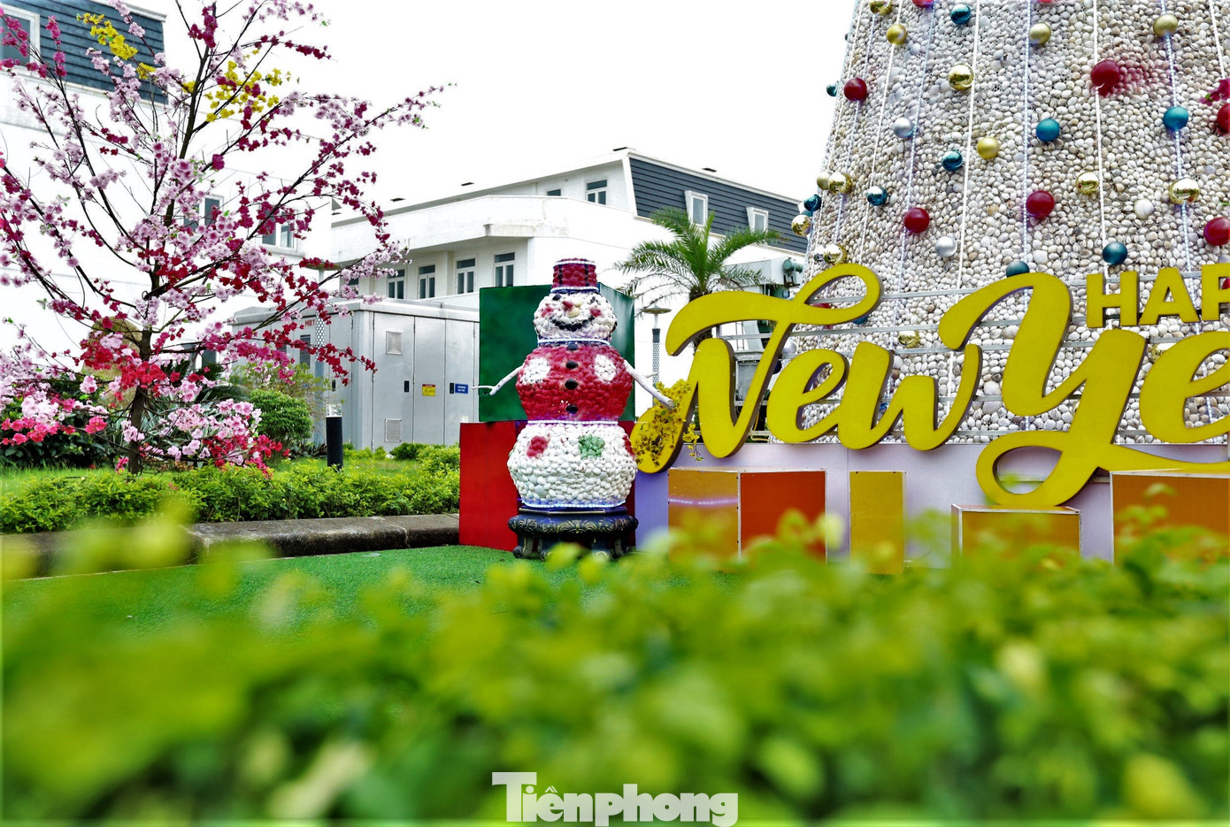 Chú người tuyết cao khoảng 1,3m dựng cạnh cây thông. Mô hình này cũng được kết dính từ vỏ sò sau đó dùng sơn nhiều màu sắc phủ lên bề mặt.