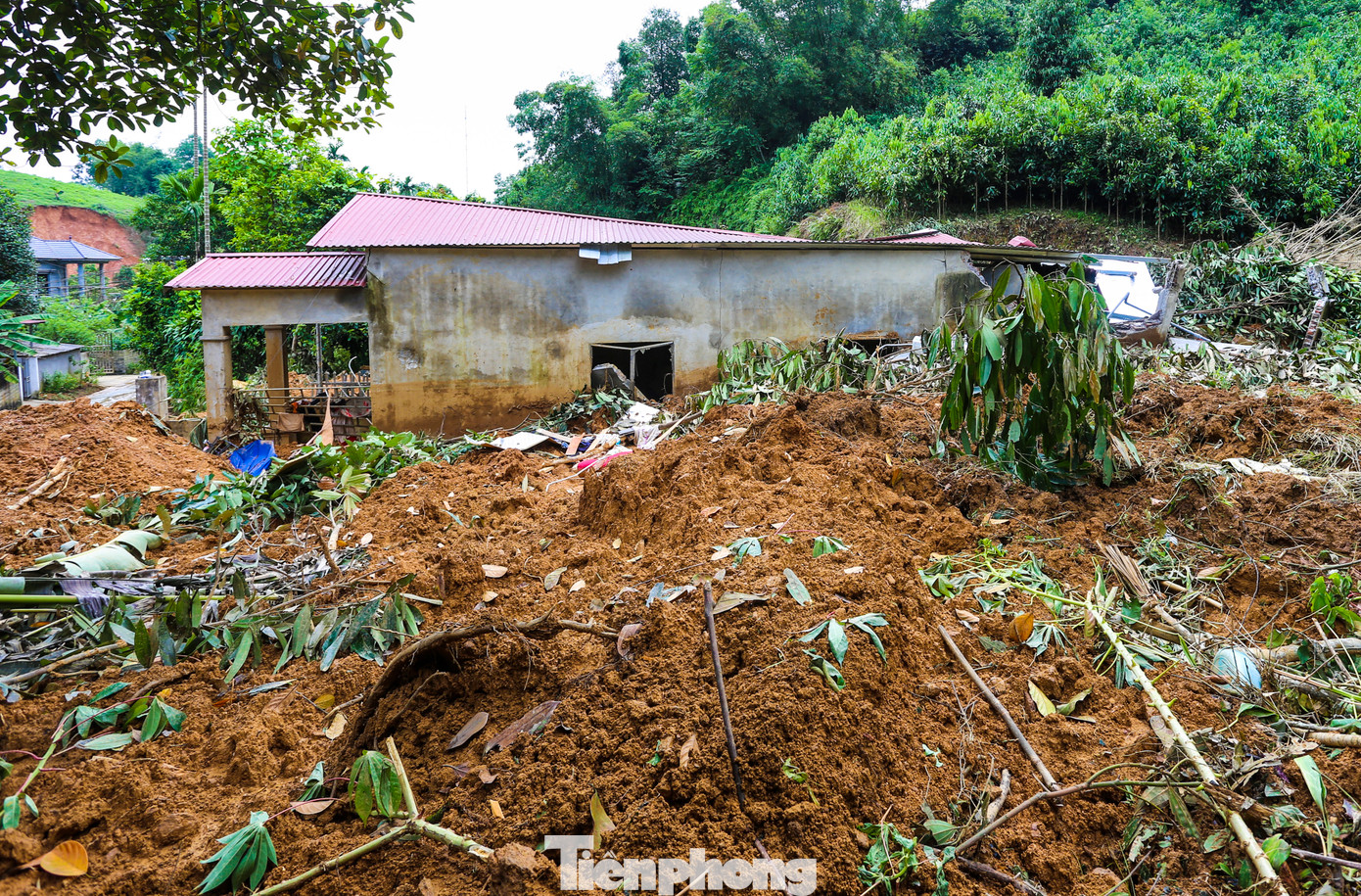 Sau vụ sạt lở, ngôi nhà xây cấp 4 phía trước vẫn còn hình hài, nhưng toàn bộ phía sau đã vỡ vụn; bùn đất, cây cối vùi lấp kín.