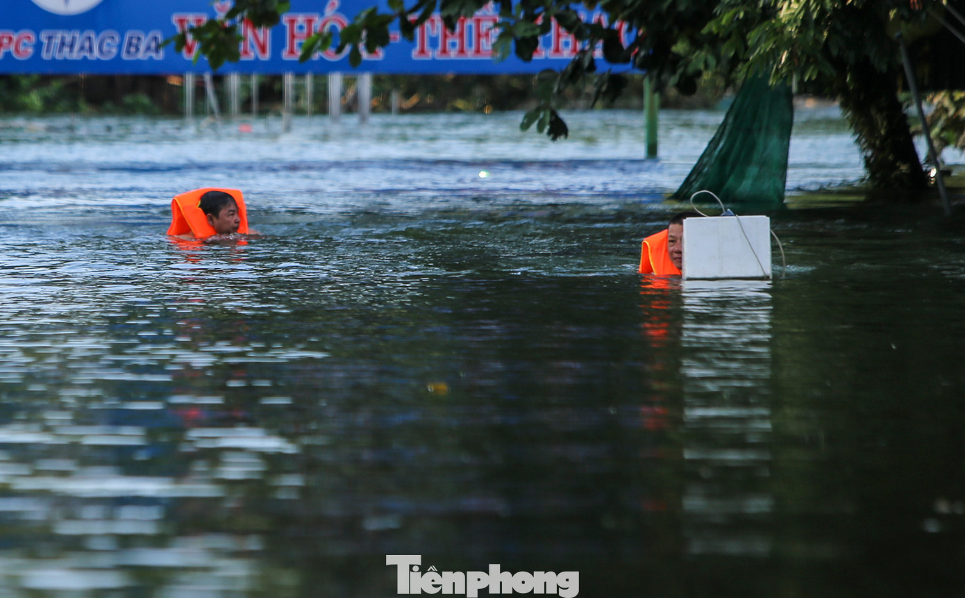 Người dân mặc áo phao, dùng thuyền hoặc di chuyển chậm cạnh khu vực nhà ngập để di dời tài sản.