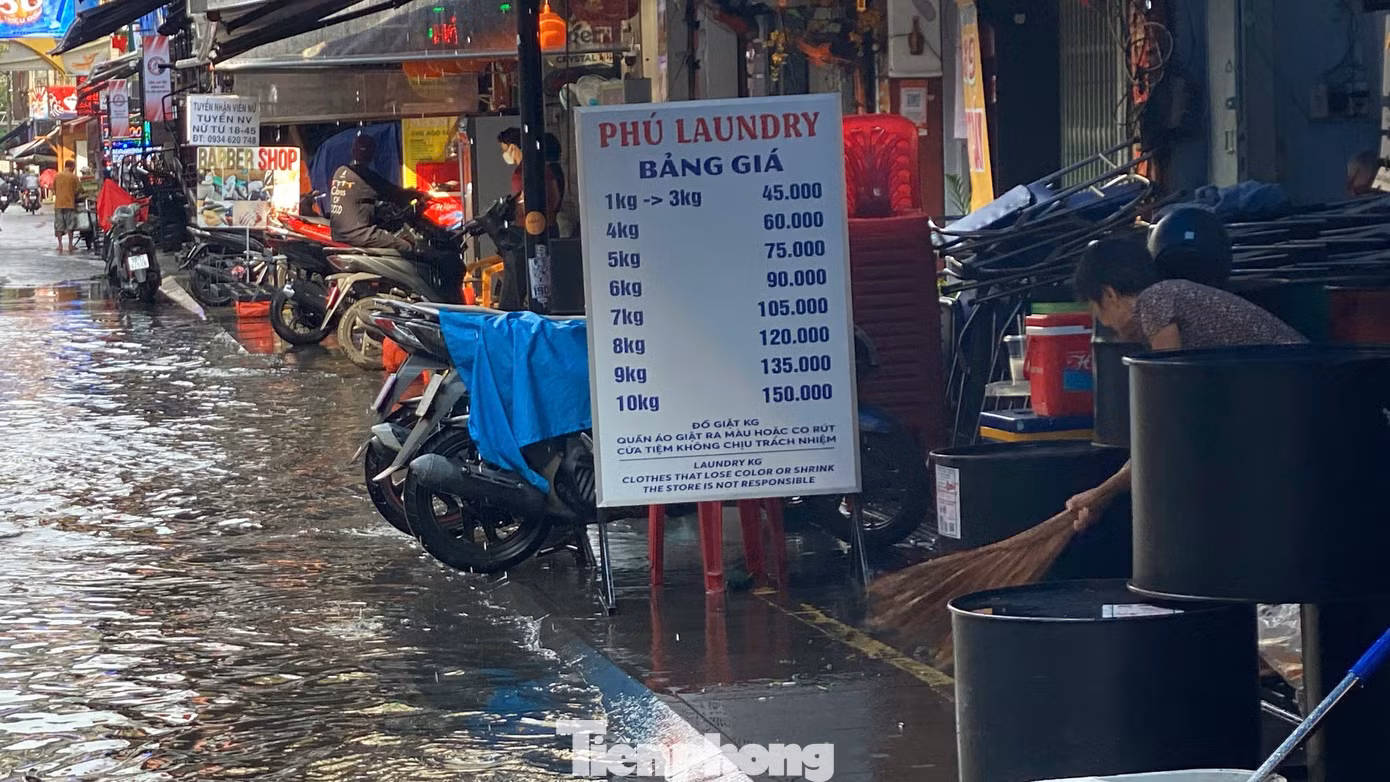 Nhân viên các hàng quán hai bên đường tất bật dọn dẹp, thu gom rác, khơi thông miệng cống để nước rút nhanh hơn.