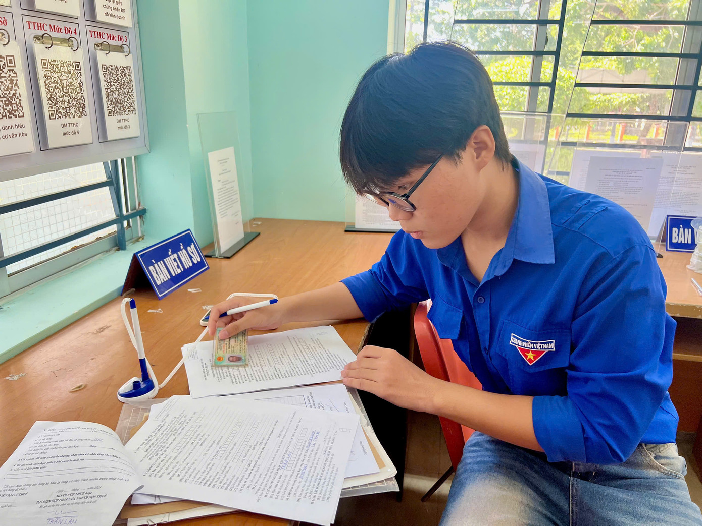 "Tôi đã lớn tuổi, tay lại run nên nhiều lần viết giấy tờ sai khiến hồ sơ bị trả về. Nay nghe tin chính quyền mới vận hành, tôi lại mang hồ sơ ra phường để làm lại.Trước khi đi tôi rất lo lắng vì sợ lại viết sai như trước. May sao có các cháu thanh niên ở đây hướng dẫn lấy số, viết giúp các mẫu tờ khai nên hồ sơ của tôi nhanh chóng được hoàn thành và đã được cán bộ tiếp nhận, xử lý”, ông Lâm xúc động nói. Trong ảnh: Thanh niên tình nguyện phường Cam Ranh, tỉnh Khánh Hòa hỗ trợ ông Lâm điền thông tin ở các mẫu tờ khai.