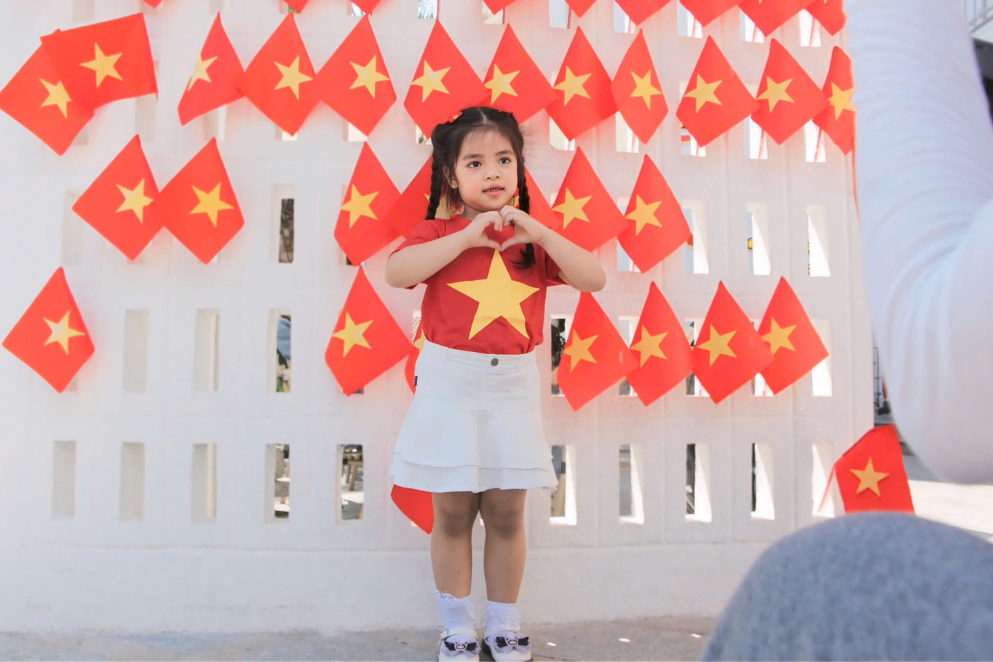 Một bạn nhỏ chụp hình kỷ niệm với bức tường cờ đỏ sao vàng đầy ấn tượng.