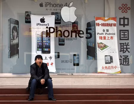 Một người đàn ông ngồi ngáp trước 1 cửa hàng bán sản phẩm của Apple tại Bắc Kinh, Trung Quốc hôm 2/4. Ảnh Reuters