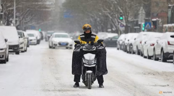 Một người giao hàng đi xe máy trên đường phố trơn trượt do tuyết rơi ở Bắc Kinh (Trung Quốc). Ảnh: Tingshu Wang/ Reuters.