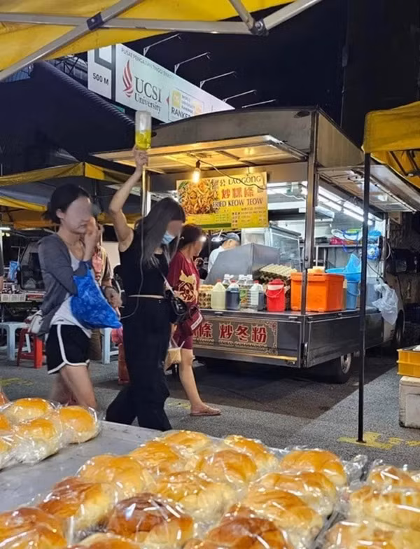Một cô gái thì nhiệt tình cầm chai truyền dịch giơ cao cho bạn đi quanh chợ đêm. Ảnh: TCNM.