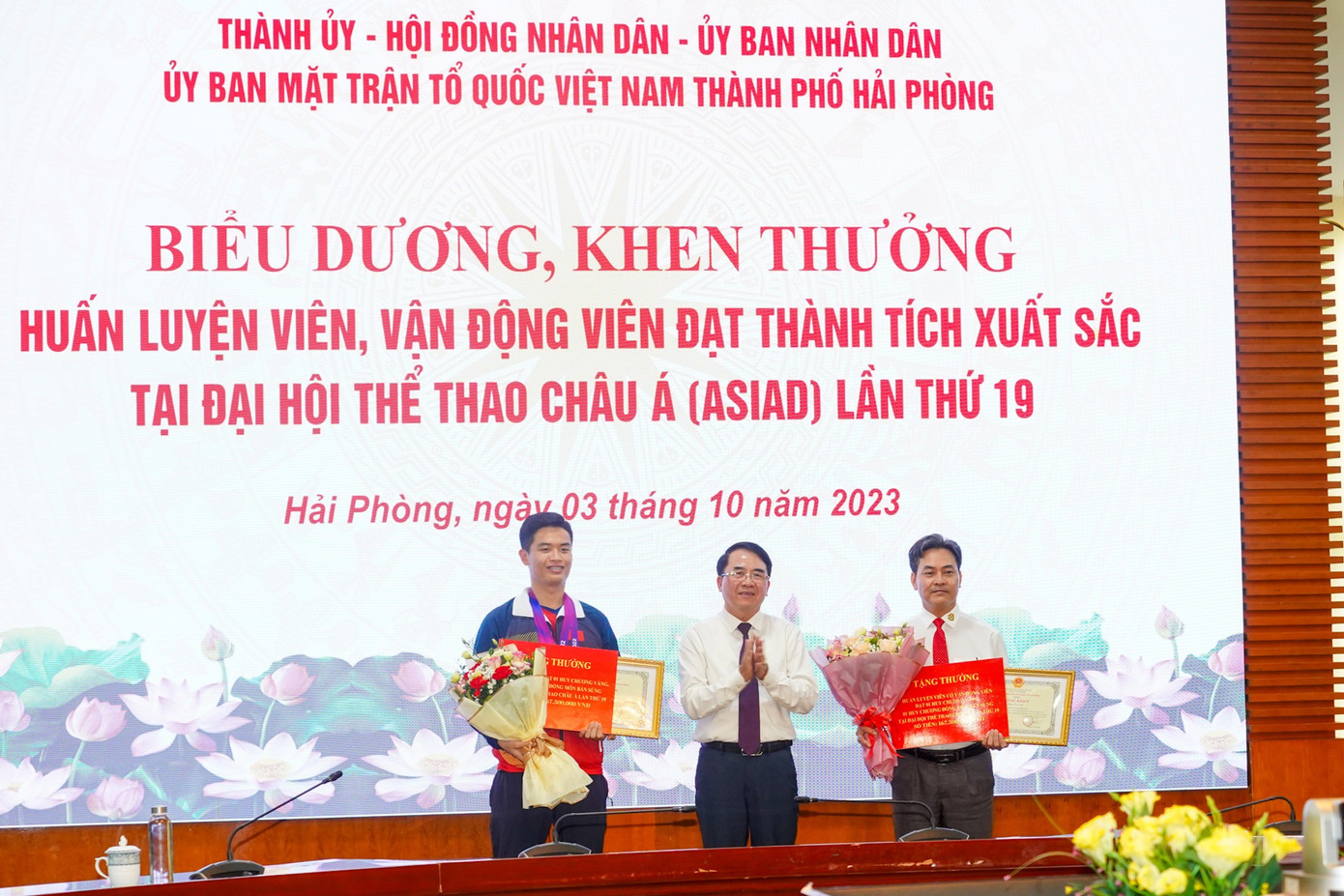 Ông Lê Khắc Nam - Phó chủ tịch UBND TP Hải Phòng trao quyết định khen thưởng, tặng hoa xạ thủ Phạm Quang Huy và HLV Phạm Cao Sơn chiều 3/10.