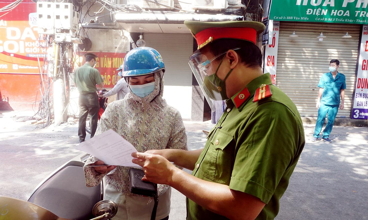Theo cán bộ tại chốt, những người ra đường thực sự cần thiết như mua lương thực, thực phẩm, thuốc men... hoặc xuất trình giấy đi làm của công ty được phép hoạt động theo Chỉ thị của UBND thành phố Hà Nội. Trong ảnh, người phụ nữ xuất trình giấy đi làm của công ty cho lực lượng chức năng.