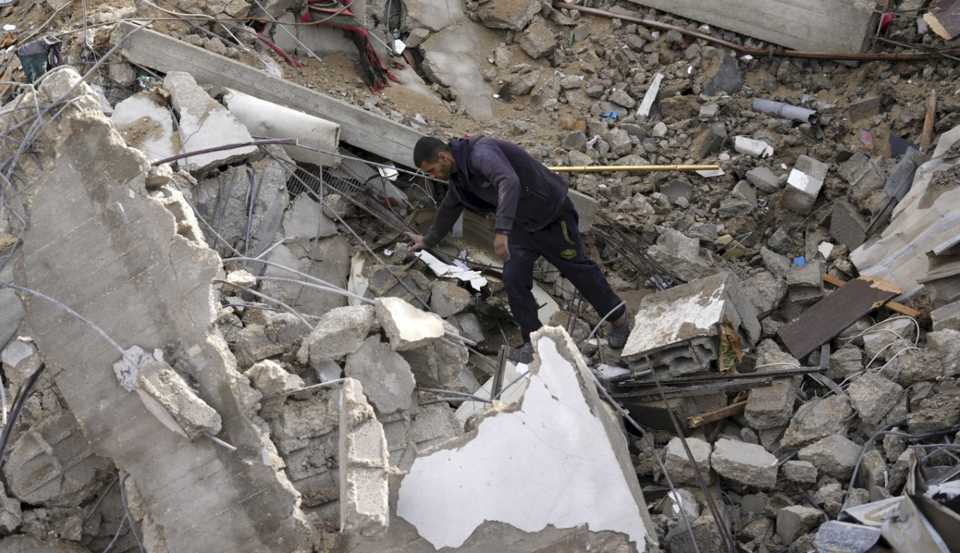 Một người Palestine tìm kiếm trong đống đổ nát sau khi cuộc không kích của Israel đánh sập tòa nhà dân cư ở Dải Gaza ngày 14/1. (Ảnh: AP)