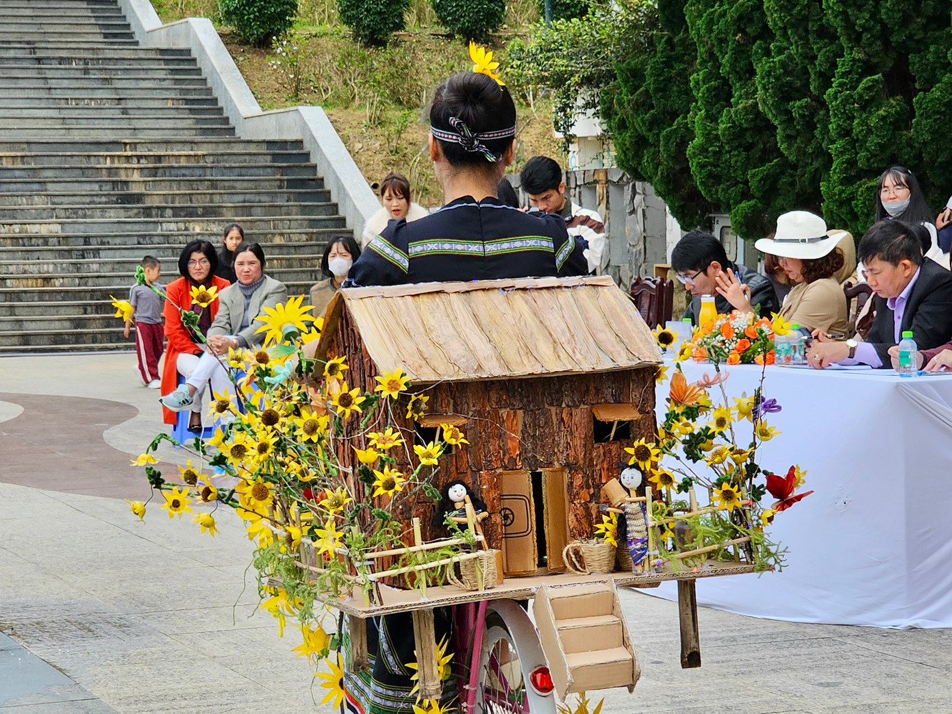 Mô hình nhà sàn, hoa dã quỳ được nữ giáo viên diện trang phục người dân tộc trường Mầm non Tà Nung trình diễn.