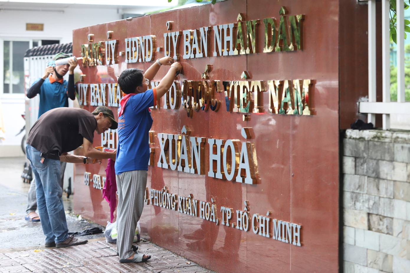 Một trong những việc làm quan trọng là thay đổi các bảng tên đơn vị hành chính cũ bằng tên phường, xã mới theo các quyết định công nhận đơn vị hành chính mới. Trong ảnh: Các nhân công thực hiện lắp đặt tên đơn vị hành chính phường Xuân Hòa thuộc TPHCM, tại địa chỉ số 99 Trần Quốc Thảo. Trước đây, địa chỉ này là trụ sở của Quận ủy, UBND quận 3. Ảnh: Ngô Tùng