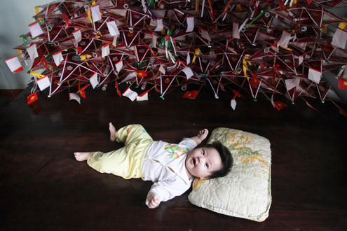 Đứa cháu ngoại thứ hai của chị Tuyến nằm chơi bên cạnh chồng đèn ông sao đã chuẩn bị cho dịp Tết thiếu nhi. Nhiều năm nay, chị được Bảo tàng Dân tộc học đặt hàng và mời hướng dẫn cho trẻ em làm các loại đồ chơi truyền thống. 