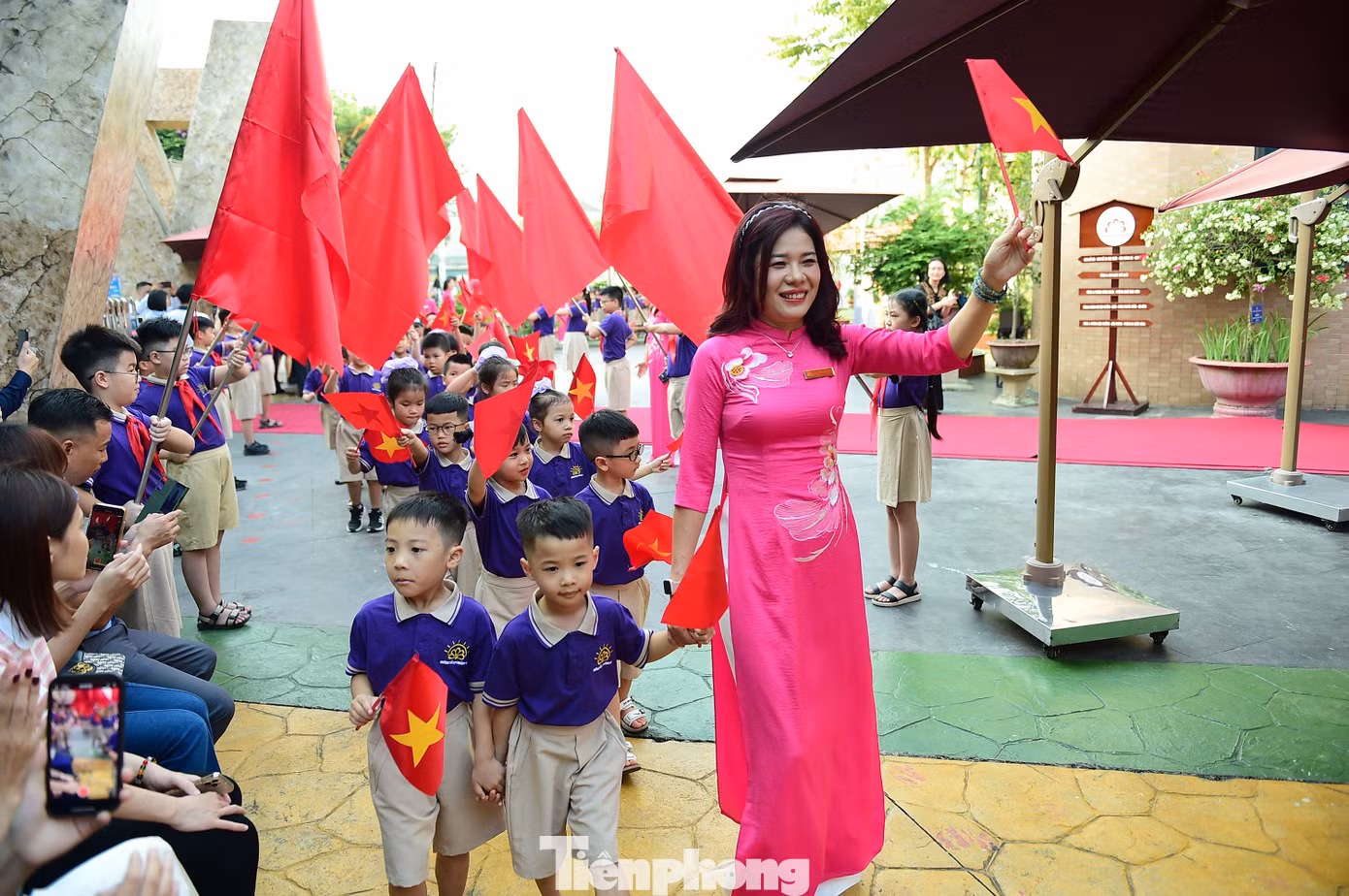 Lễ khai giảng năm học mới càng thêm đặc biệt với các bạn nhỏ bước vào lớp 1. Trong ảnh, các em học sinh lớp 1 trường Tiểu học Hoàng Mai (Hà Nội) tay vẫy cờ đỏ sao vàng và hoa, được giáo viên chủ nhiệm dẫn bước vào trường. Ảnh: Xuân Tùng