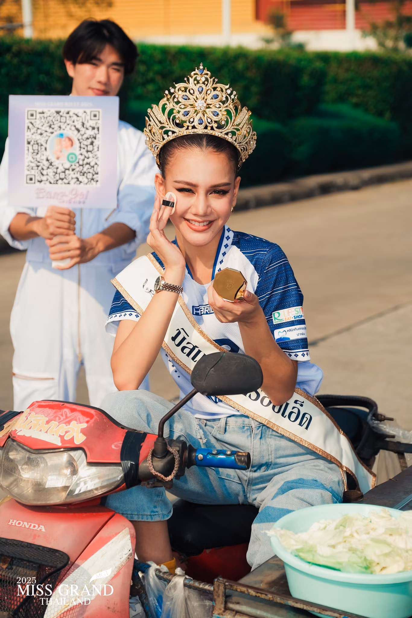 Một người đẹp lái xe máy đến địa điểm dự thi. Cô đeo vương miện, sash và trang điểm ngay trên xe.