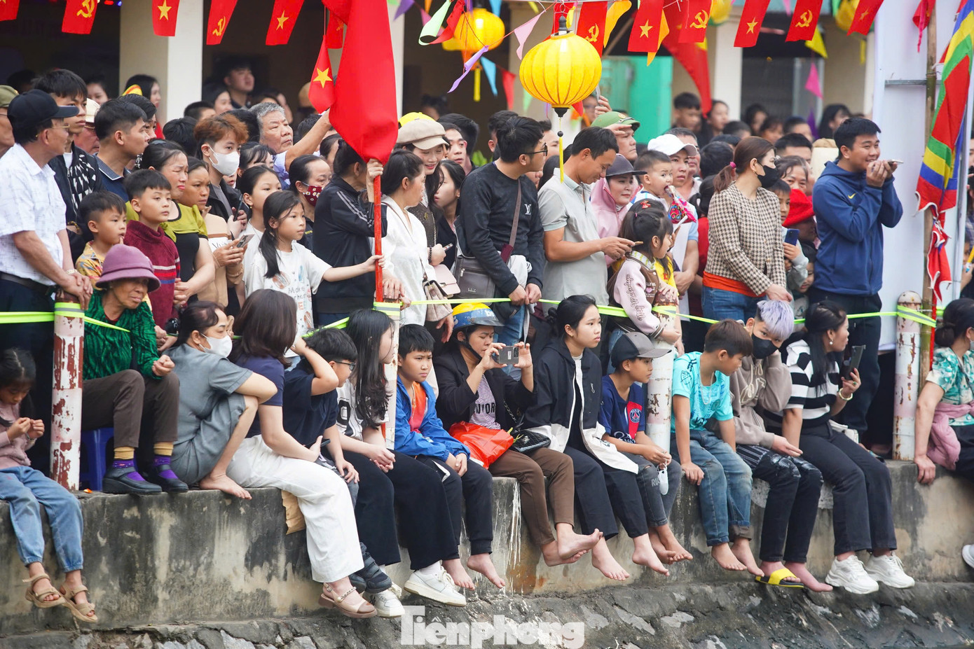 Nhiều người ngồi tràn qua cả lan can bảo vệ của bờ sông, trong đó.có không ít trẻ nhỏ. Điều này gây nhiều nguy cơ mất an toàn nếu người dân chen lấn, xô đẩy để tiến sát bờ sông, cổ vũ cho đội bơi thuyền mình yêu thích.