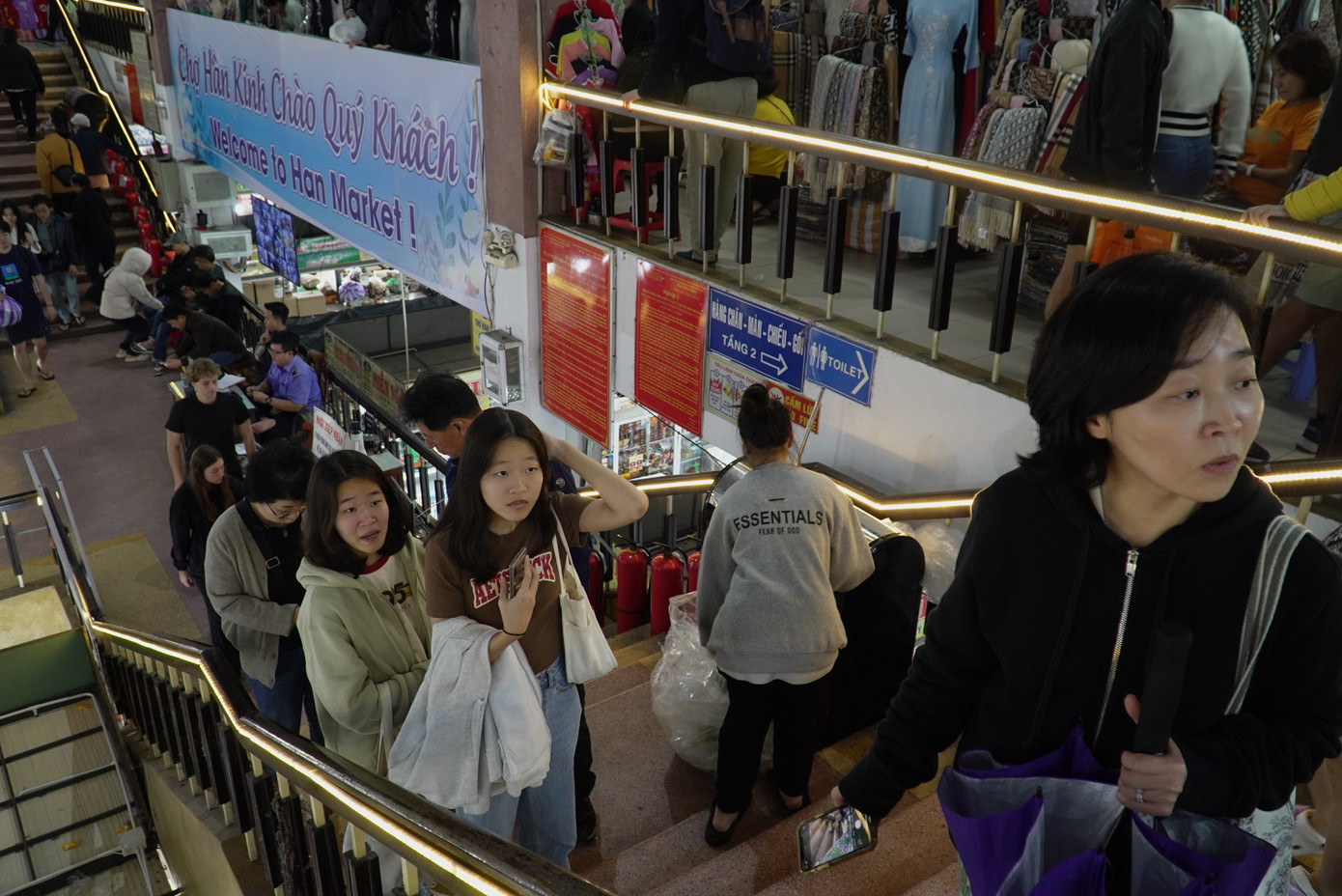 Du khách nối nhau lên tầng hai mua sắm quần áo, giày dép. Các lối đi chật kín, phải nép người nhường nhau. Các tiểu thương chia sẻ hiện các loại giày, dép đi mưa bán chạy hơn do Đà Nẵng mưa liên tục. Ảnh: Thanh Hiền.