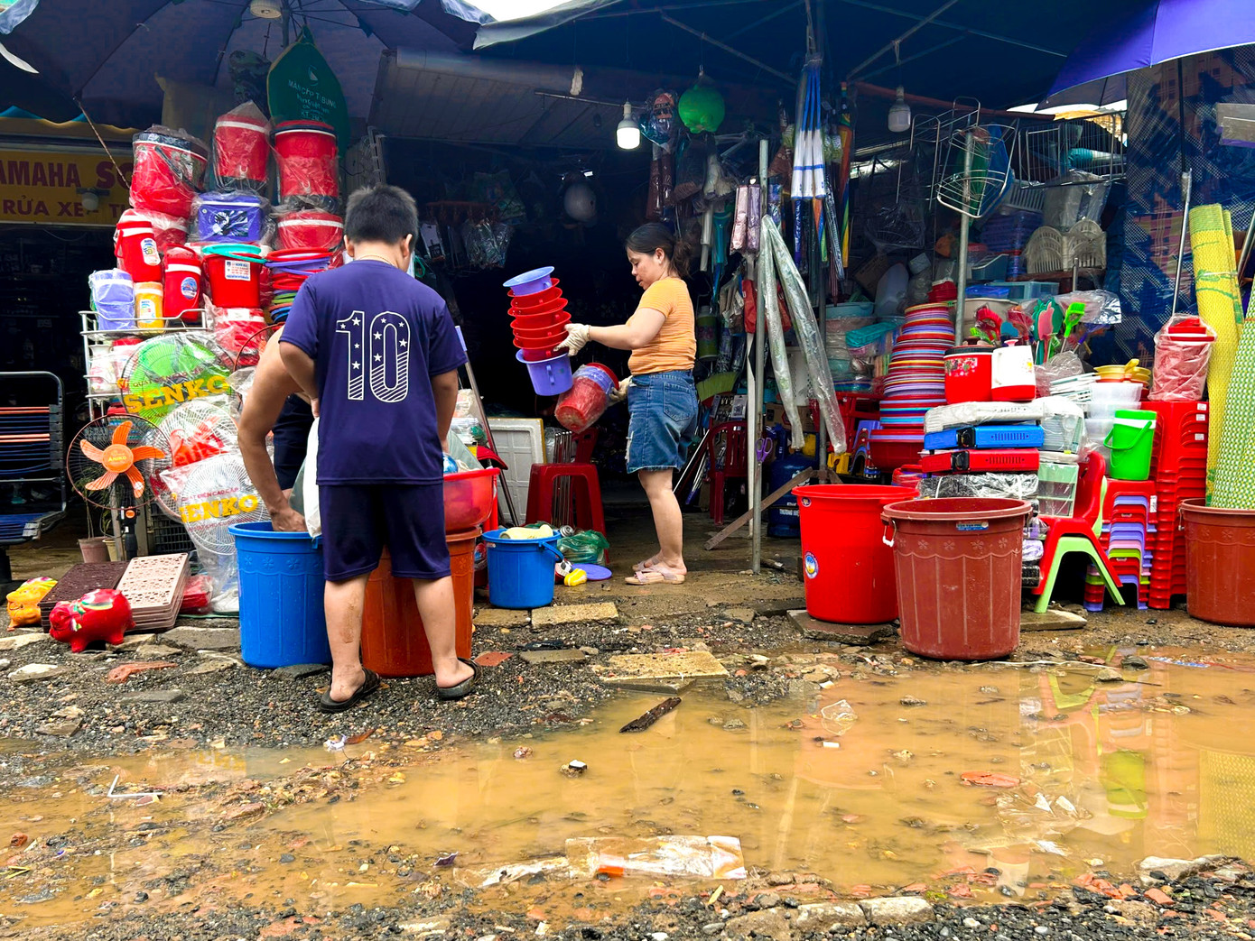 Nước từ các khu vực cao đổ về nhanh và chảy xiết, khiến hàng loạt quầy hàng trong chợ bị ngập. Nhiều tiểu thương trở tay không kịp, một số mặt hàng bị cuốn trôi, bùn đất theo dòng nước tràn vào bên trong chợ.