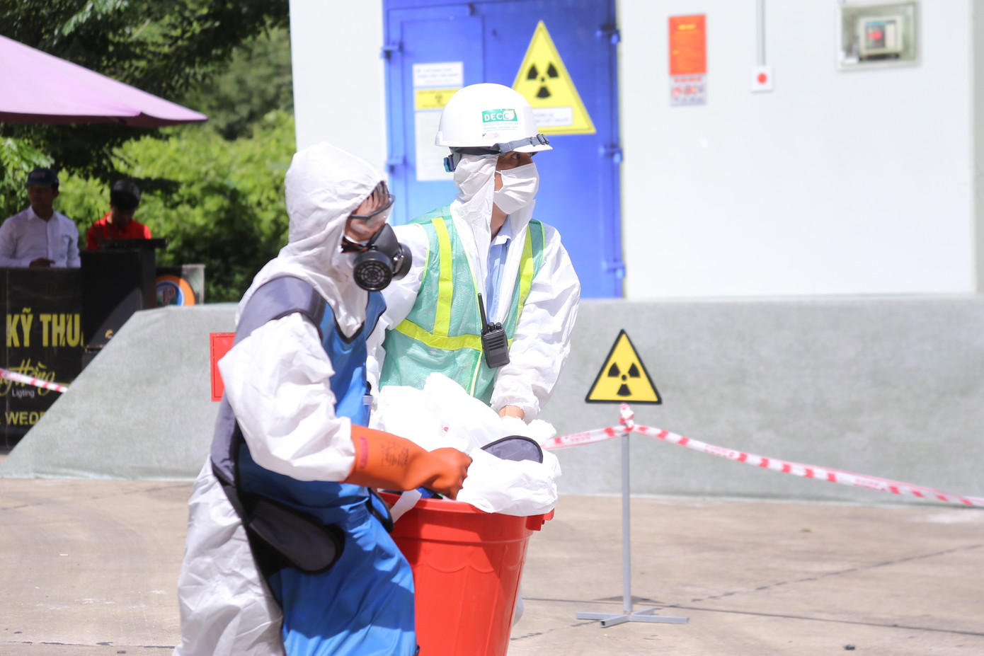 Sau khi kết thúc tẩy xạ, các lực lượng ứng phó hiện thu nguồn phóng xạ và di chuyển các thùng chì chứa chất nhiễm phóng lên xe và đưa đi xử lý.