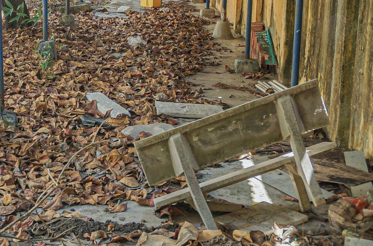 Phía bên ngoài hành lang nhiều bàn ghế vứt bừa bãi, lá cây phủ kín khuôn viên tạo nên khung cảnh nhếch nhác, hoang tàn. Phía bên ngoài hành lang nhiều bàn ghế vứt bừa bãi, lá cây phủ kín khuôn viên tạo nên khung cảnh nhếch nhác, hoang tàn.