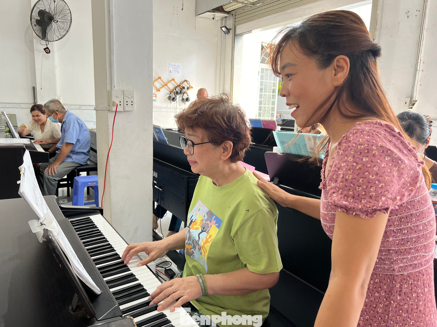 Cô Trần Thị Thọ (đứng), người sáng lập Trung tâm Upponia tâm sự, trước đây trung tâm chủ yếu dạy nhạc cho các em nhỏ. Không ít lần nghe tâm sự về niềm yêu thích âm nhạc của những người ông, người bà khi đưa con cháu mình đến lớp, cô Thọ quyết định mở thêm lớp dạy piano miễn phí cho người cao tuổi.