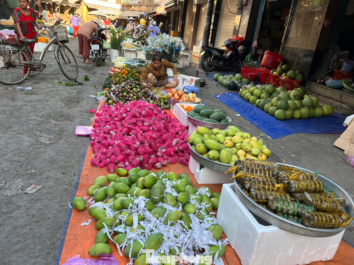 Trái cây đổ ngay dưới lòng đường, giá giảm hơn so với những ngày cao điểm cận Tết. Giá vú sữa là 25.000 đồng/kg, xoài là 20.000 đồng, dưa hấu là 15.000 đồng/kg, cam quýt có giá từ 35.000 đồng/kg; bánh tét có giá từ 40.000 đồng/đòn...